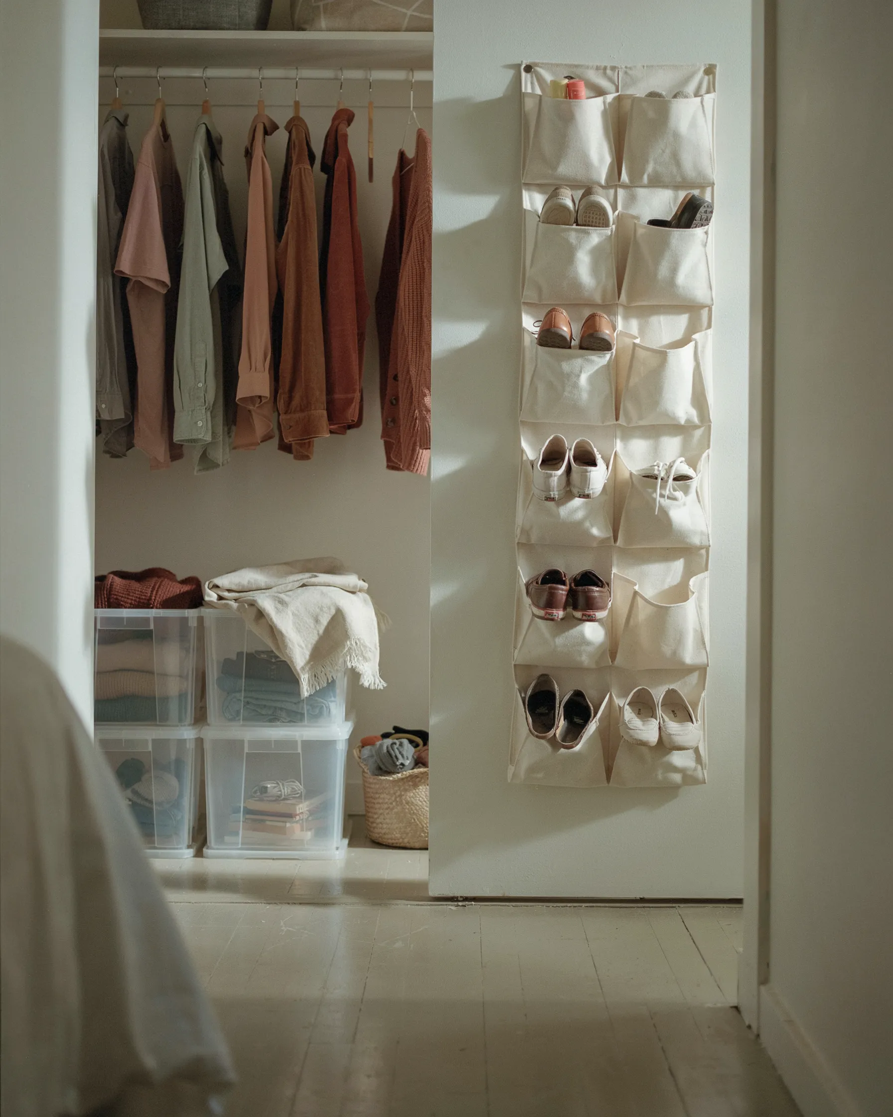 Dorm closet with hanging clothes, stackable clear storage bins, and a canvas shoe organizer with shoes hanging on the door