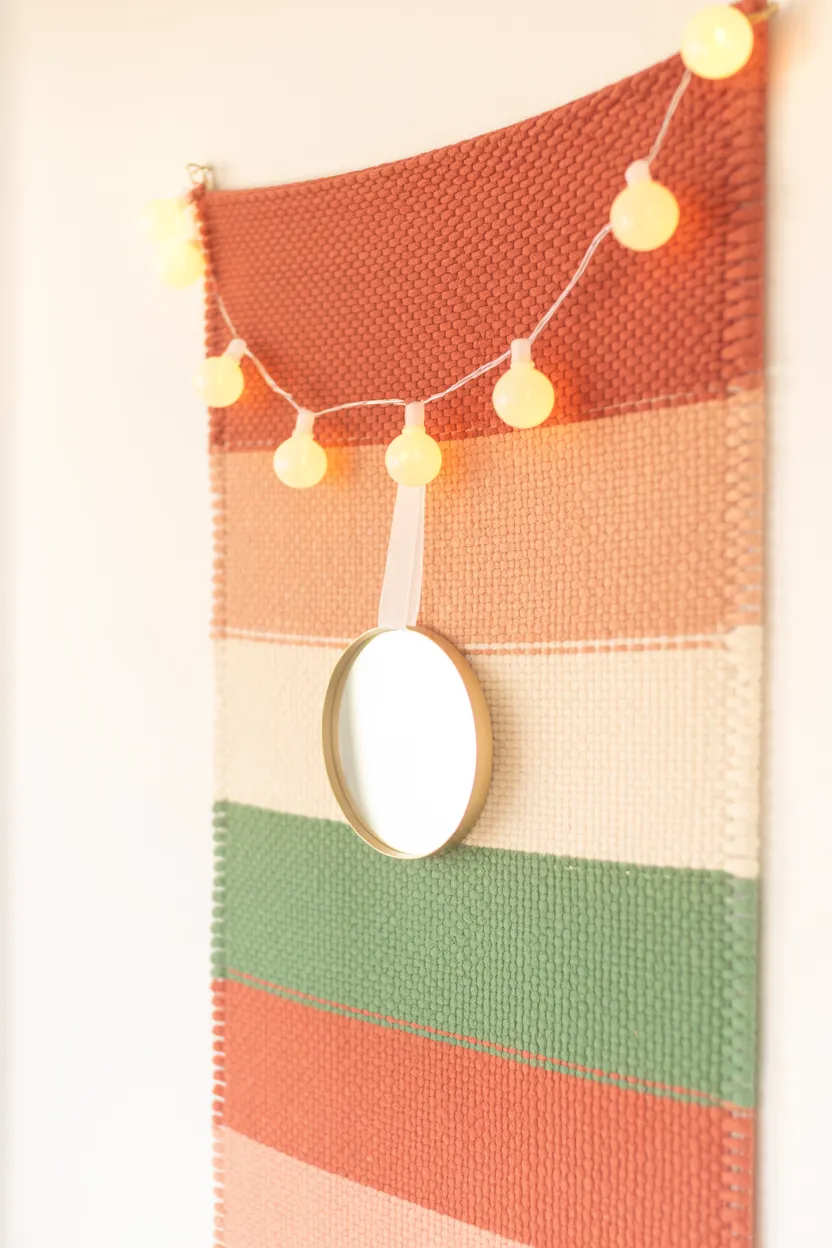 Dorm room wall decorated with a fabric tapestry, warm battery string lights, and a small adhesive mirror, hung with command strips